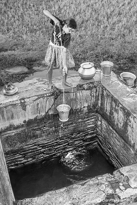 A young girl procuring water from a Paata Daarhi situated in paddy fields in Khunti district, Jharkhand, India